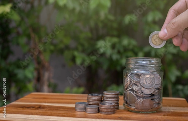 Fototapeta coin saving hand on wooden table and natural background saving money for future retirement or investment