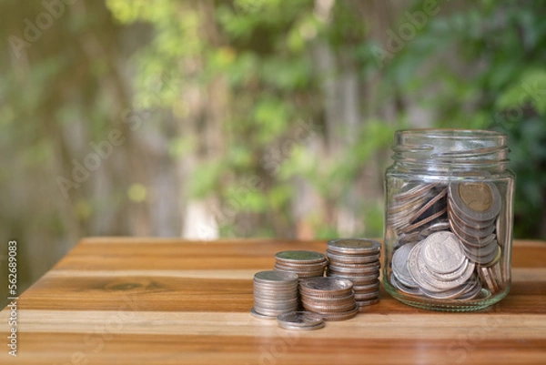 Fototapeta coin stacking on wood table and in side jar with natural background, concept of financial and money saving