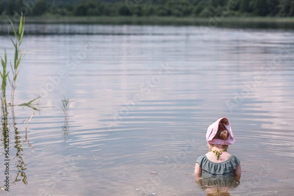 Fototapeta A little girl of three years old bathes in a forest lake in the summer.