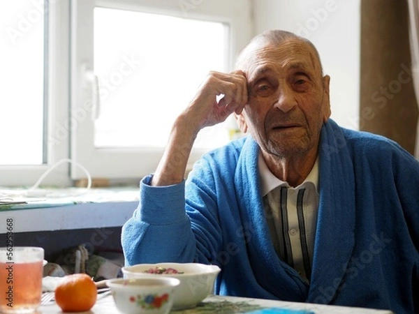Fototapeta Close up portrait of 92 year old grandfather. Grandpa sits at the table in his room and stares into the camera. Care and everyday life of the elderly.