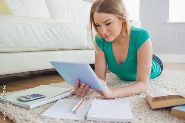 Fototapeta Attractive woman lying on floor using tablet to do her homework
