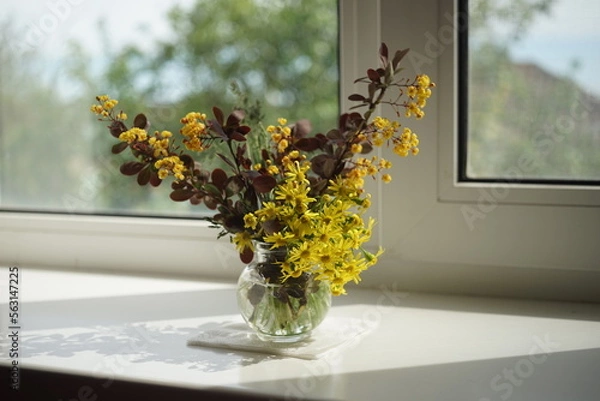 Fototapeta The branches of barberry bush with blooming yellow flowers in a glass vase on the windowsill
