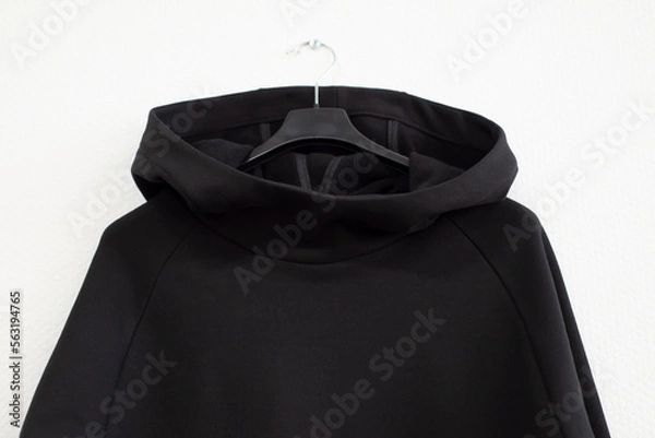 Fototapeta Stylish black sweater with a hood on a white background, front view. Urban clothing made of knitted footer hangs on hangers. Place for text. Mocap.
