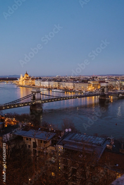 Fototapeta Night view of Budapest showcasing illuminated buildings, bridges, and reflections on the Danube River at dusk