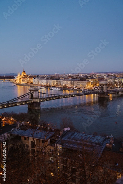 Fototapeta Night view of Budapest showcasing illuminated buildings, bridges, and reflections on the Danube River at dusk