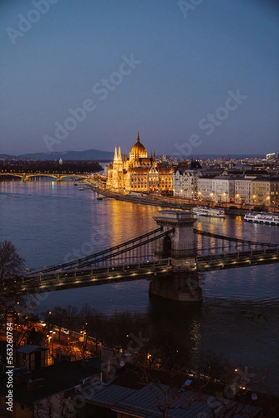 Fototapeta Night view of Budapest showcasing illuminated buildings, bridges, and reflections on the Danube River at dusk