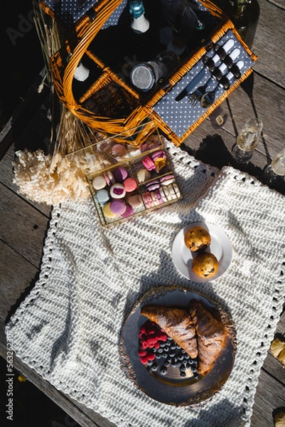 Fototapeta Picnic basket with bakery, fruits and sweets on white blanket.