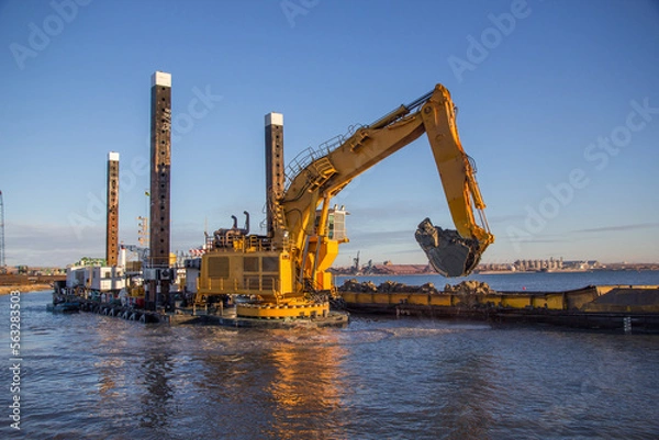 Fototapeta In the port, a large floating dredging excavator scoops up soil from the bottom