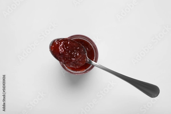 Fototapeta Spoon with tasty canned raspberry jam on jar against white background, top view