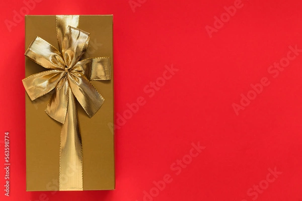 Fototapeta Golden gift box with golden ribbon and bow on a red background. Top view. Copy space.