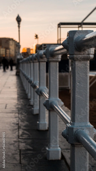Fototapeta Vertical photo of Gijon city walkway white fence at golden hour with sbeach close to the walkway, placed in Asturias, Spain.