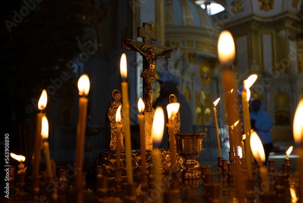 Fototapeta Cross with crucifix in focus, lit wax candles, funeral service, prayers for salvation of soul. Memorial service, an Orthodox church. Concept of Christian religion.