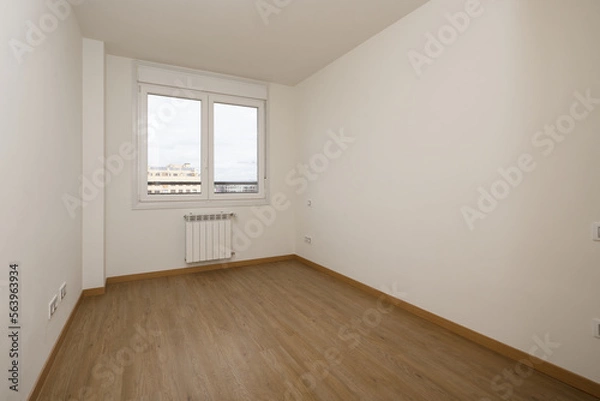 Obraz Empty room of a house with a dark colored laminate floor and a white aluminum window with two panes and a view of the city