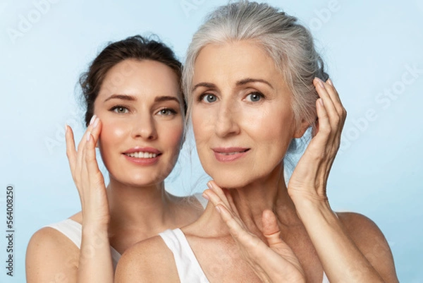 Fototapeta Two women of different ages and skin types take care of their facial skin, apply moisturizer, and look at the camera
