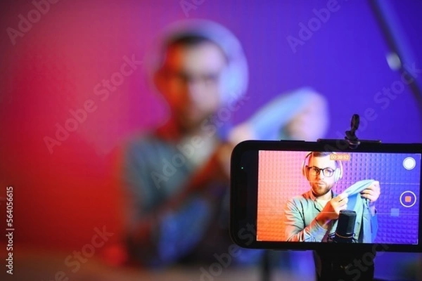 Fototapeta Panoramic view of young adult vlogger creating internet content, holding carton box in hands, unpacking received pack and recording media online video on broadcast equipment