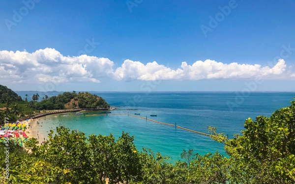 Fototapeta The view from Ilha dos Frades, Salvador, Bahia, Brazil shows a picturesque beach in a crystal-clear bay, with vibrant blue hues and fluffy clouds.