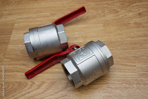 Fototapeta Two large two-inch ball valves with a red lever handle lie on the table
