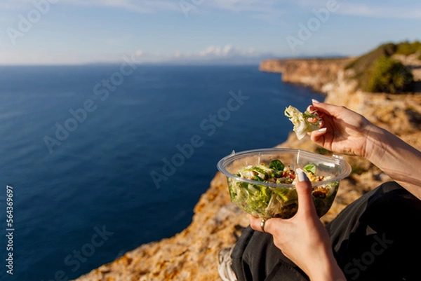 Obraz Woman eating a salad on a cliff with a beautiful seascape