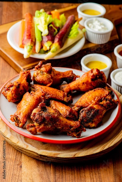 Fototapeta 
Chicken wings. Buffalo chicken wings. American cuisine of chicken wings deep-fried, dipped in buffalo sauce made of vinegar,  cayenne hot sauce and butter. Served with celery, carrots, blue cheese.