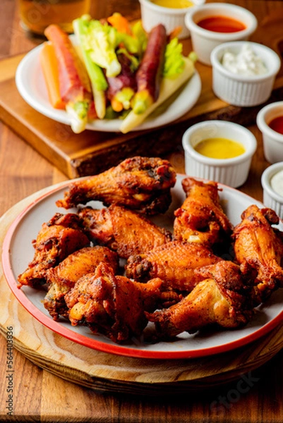 Fototapeta 
Chicken wings. Buffalo chicken wings. American cuisine of chicken wings deep-fried, dipped in buffalo sauce made of vinegar,  cayenne hot sauce and butter. Served with celery, carrots, blue cheese.