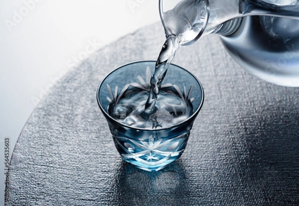 Fototapeta Sake poured into a faceted glass against a black background.