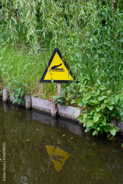 Obraz A yellow sign near the pond tells that there is a crocodile under the water. Beware of the dangerous crocodiles in Europe