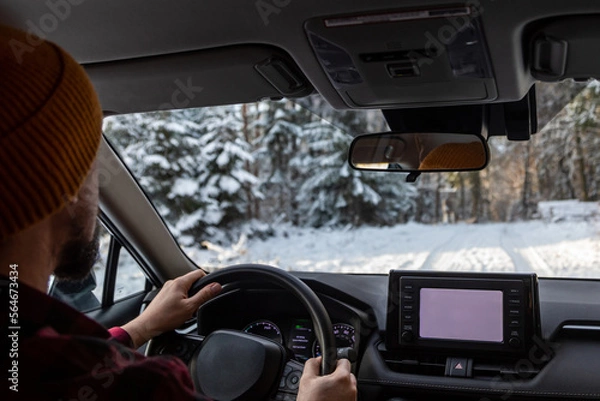 Fototapeta man driving a car on an winter road in forest. Close-up of hands on a steering wheel. view from the driver's back.