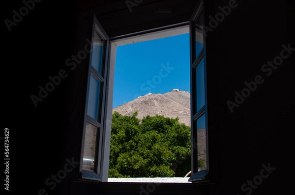 Fototapeta Looking through a window at a tree and hill on the greek island of Santorini during the day