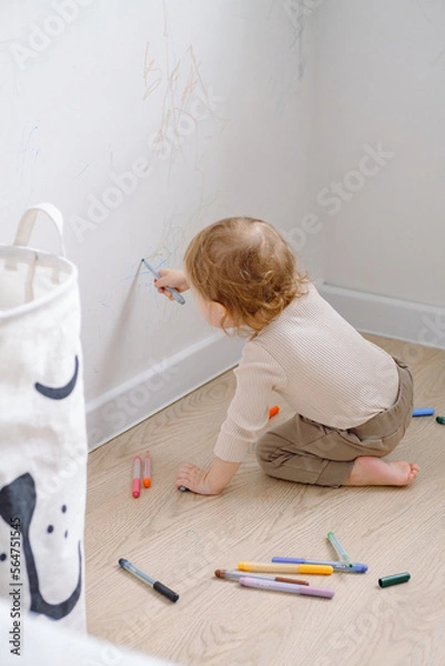 Fototapeta One year child scribbling on white wall at home. Little kid drawing on walls by colored markers. Art therapy, normal development. 