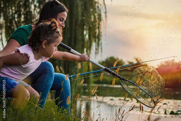 Fototapeta Catching the fish. Mom and daughter trying to catch the fish from the river. Selective focus. Side view.