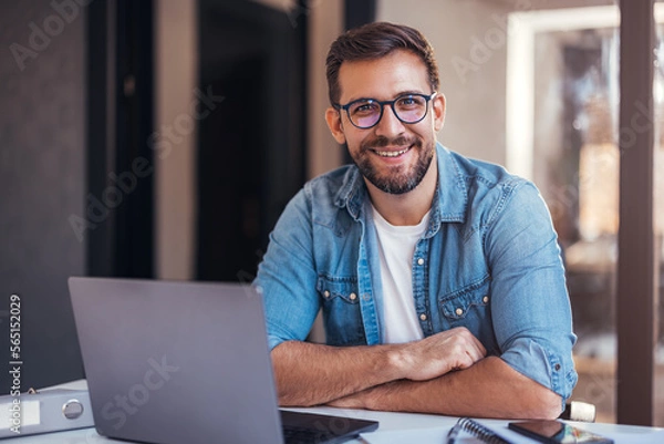 Obraz Portrait of attractive smiling man sitting in office and looking at camera.