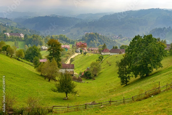 Fototapeta Rural idyllic landscape of the small villages in the Rucar-Bran mountain area, Brasov, Romania, scattered on the wooded hills, with the Bucegi mountains in the background, in wonderful springtime day