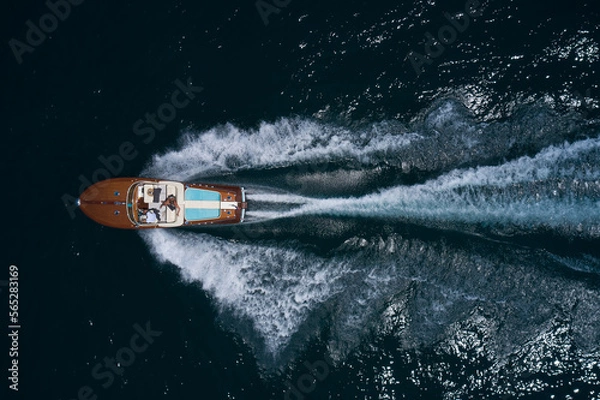 Fototapeta luxury wooden big motorboat with people fast moving on dark water top view