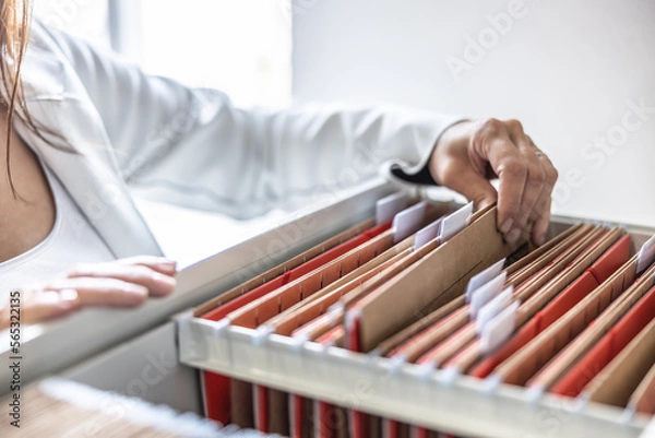 Obraz The clerk is leafing through stored folders, looking for a file or document. Concept of data storage, filing cabinet and business administration.