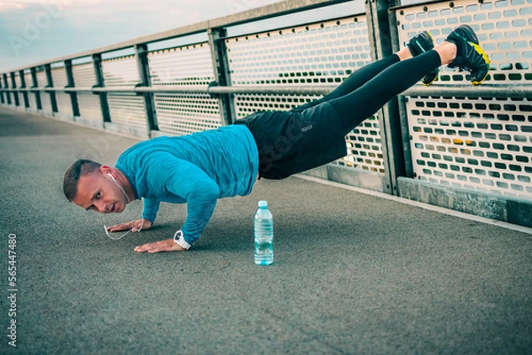 Fototapeta A man have a Training at the bridge, stretching muscles and exercising. Athlete person.