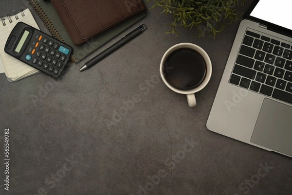 Fototapeta Laptop computer, coffee cup, calculator and notebook on black slate stone background. Flat lay, Top view