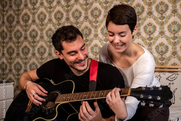 Fototapeta Young man is teaching his girlfriend to play guitar. Couple life and fun concept.
