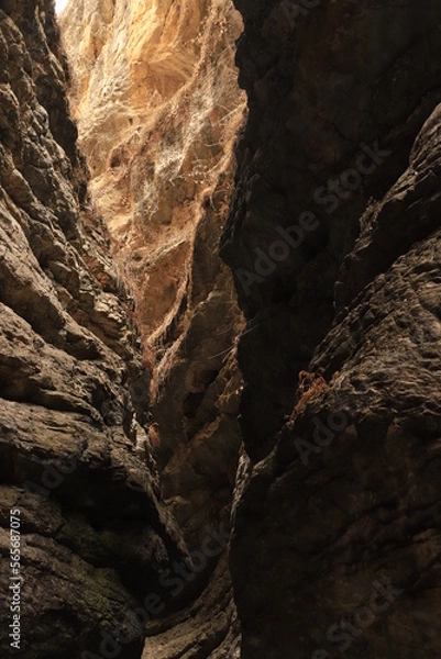 Fototapeta Bizarre shapes in a dark mountain gorge - with layers illuminated by the sun.
