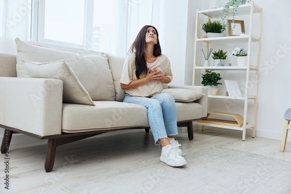 Fototapeta Woman sitting on sofa at home arm and shoulder pain, muscle sprain and joint pain, calcium problems in bones
