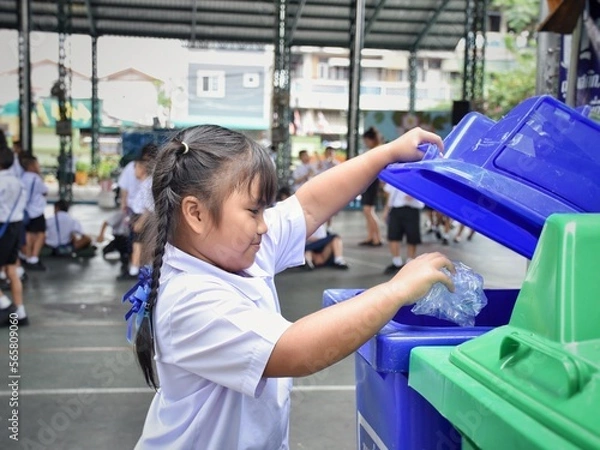 Fototapeta Elementary school students are throwing garbage into the bin with a smiling face.