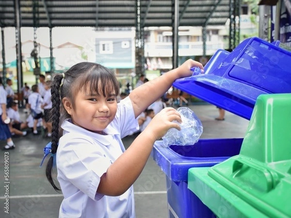 Fototapeta Elementary school students are throwing garbage into the bin with a smiling face.