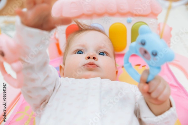 Fototapeta Adorable baby toddler lying on a colorful children's play mat with toys. Space for early development and activity of the child. baby 6 months
