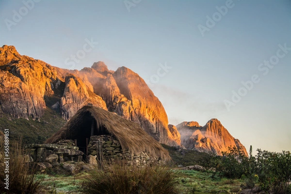 Obraz Andringitra National Park during the sunrise. Stone hut with tratched roof with rocky mountaind in the background with morning sun. Madagascar. 