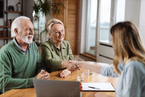 Fototapeta Happy senior woman shaking hands with a financial advisor after they came to an agreement at home