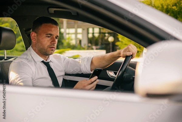 Fototapeta Businessman in a car. Work on the road. Using smartphone and laptop computer.