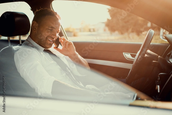 Fototapeta Businessman in a car. Work on the road. Using smartphone and laptop computer.