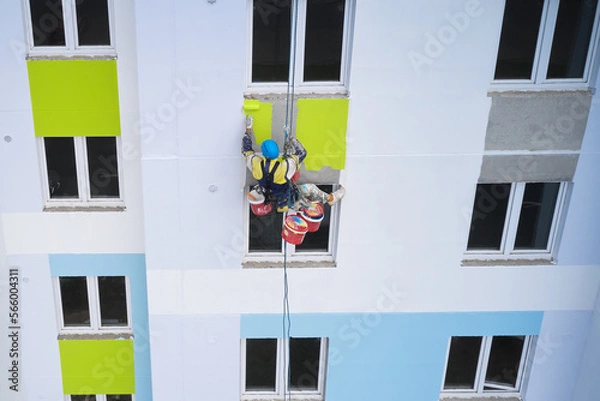 Fototapeta An industrial climber paints the facade of a multi-story building with colorful facade paints. Drone photography.
