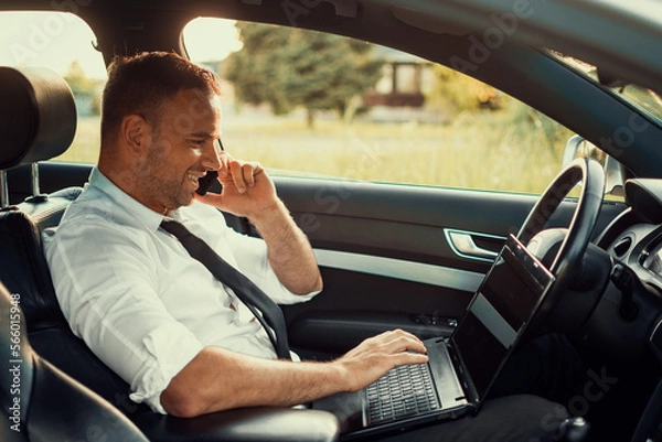 Fototapeta Businessman in a car. Work on the road. Using smartphone and laptop computer.