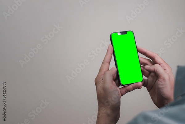 Fototapeta mock up picture of hand using mobile phone with green screen empty space