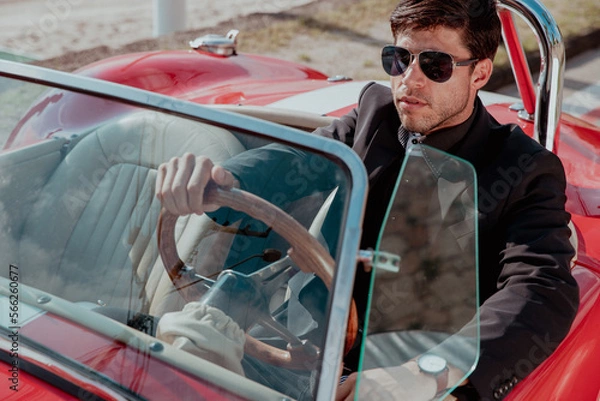 Obraz young man in convertible car looking at camera, smiling, man wears suit and tie drives red convertible car